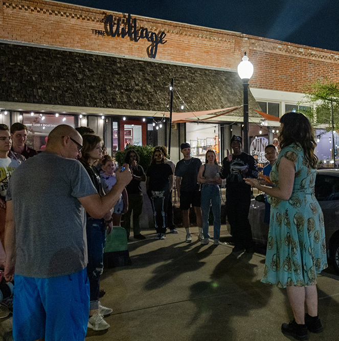 A theater instructor addresses a crowd gathered around her outside of a cafe.