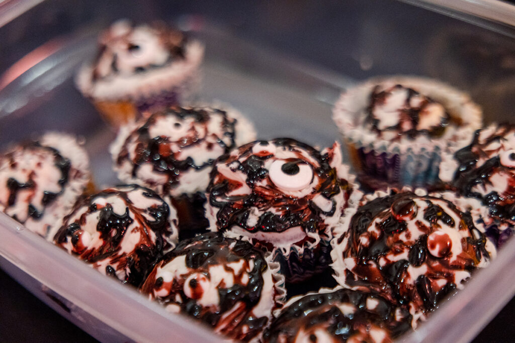 A plastic container with cupcakes inside, drizzled in red chocolate, white icing and eyeball toppings.