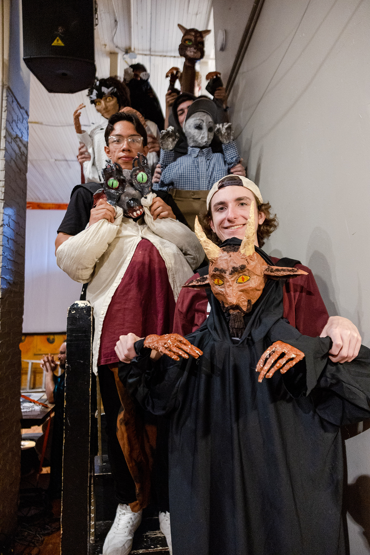 A group of college students stand on a staircase, each holding a puppet they made that connect to local folklore stories.