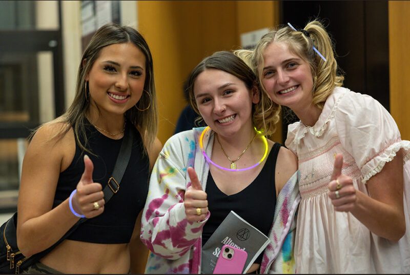 Three college students give a thumbs-up gesture.