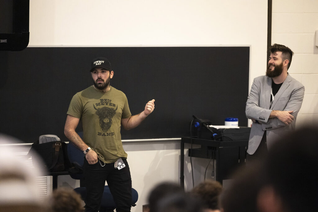 Two music performers speak in front of college students in a classroom.