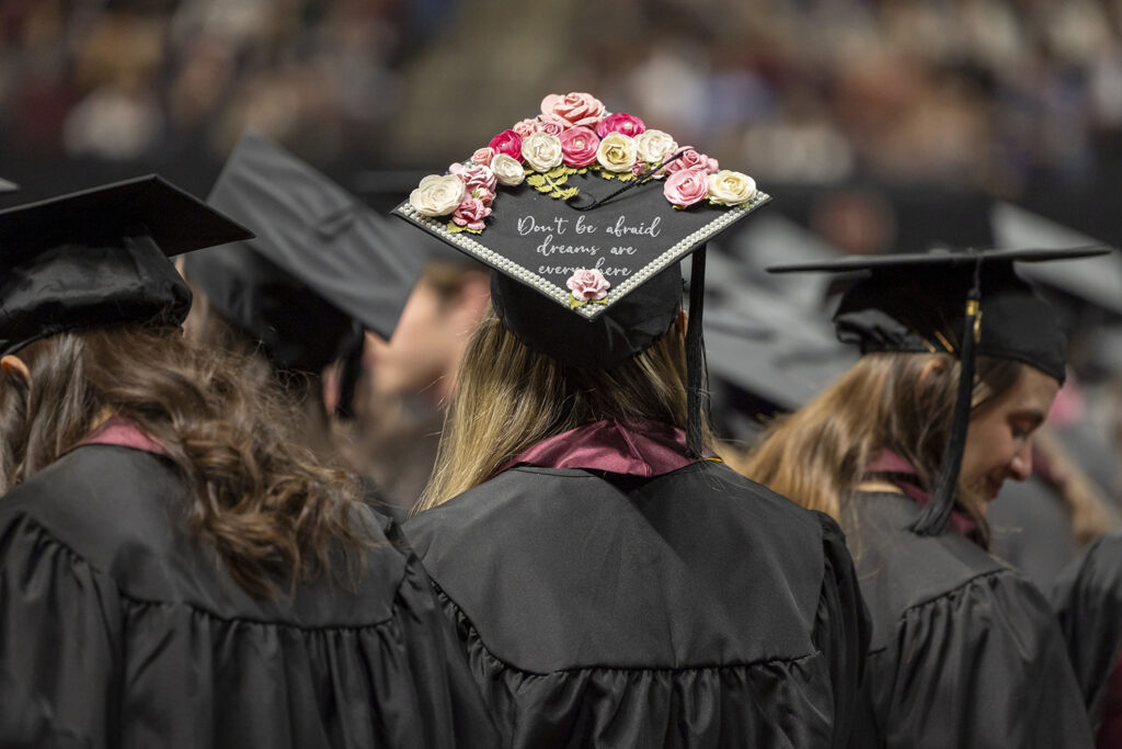 The back view of a graduating college student's mortar board, which is decorated with flowers and the words "Don't be afraid, dreams are everywhere."