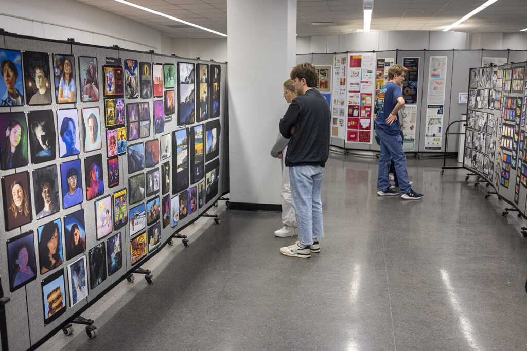 College students examine colorful works of art during a college art show.