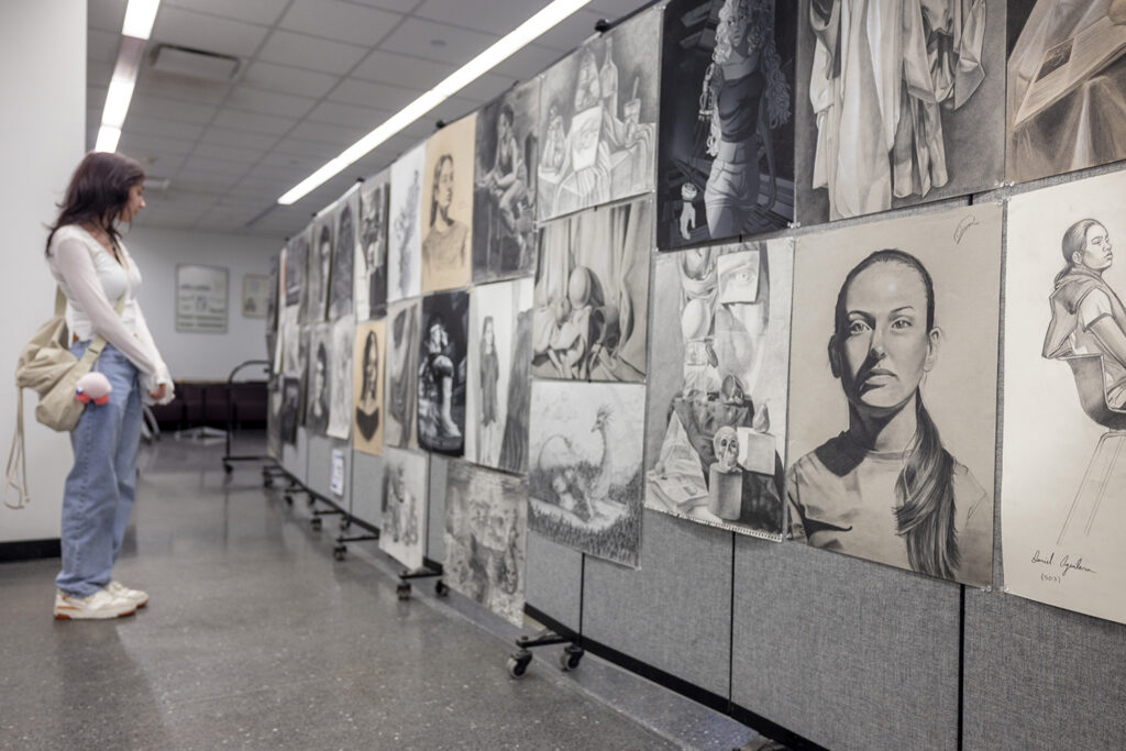 A college student examines black and white drawings and artwork during a college art show.