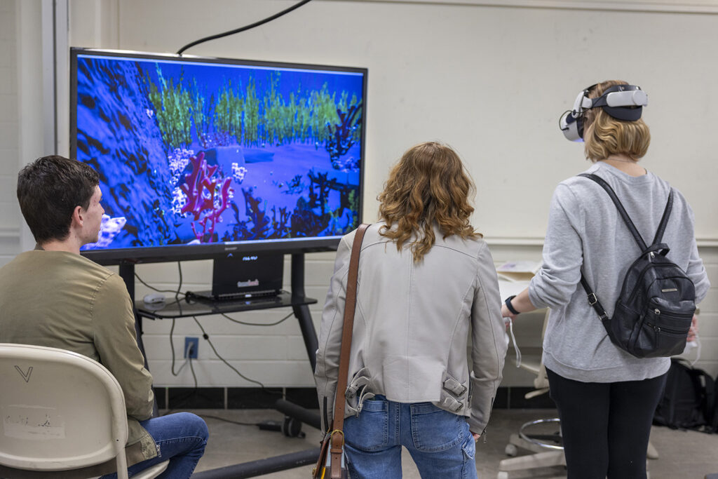 A woman engages with a virtual reality game while two people watch.