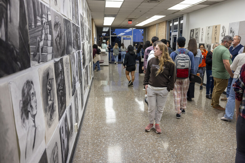 Visitors examine art hung in the hallway during a college art show.