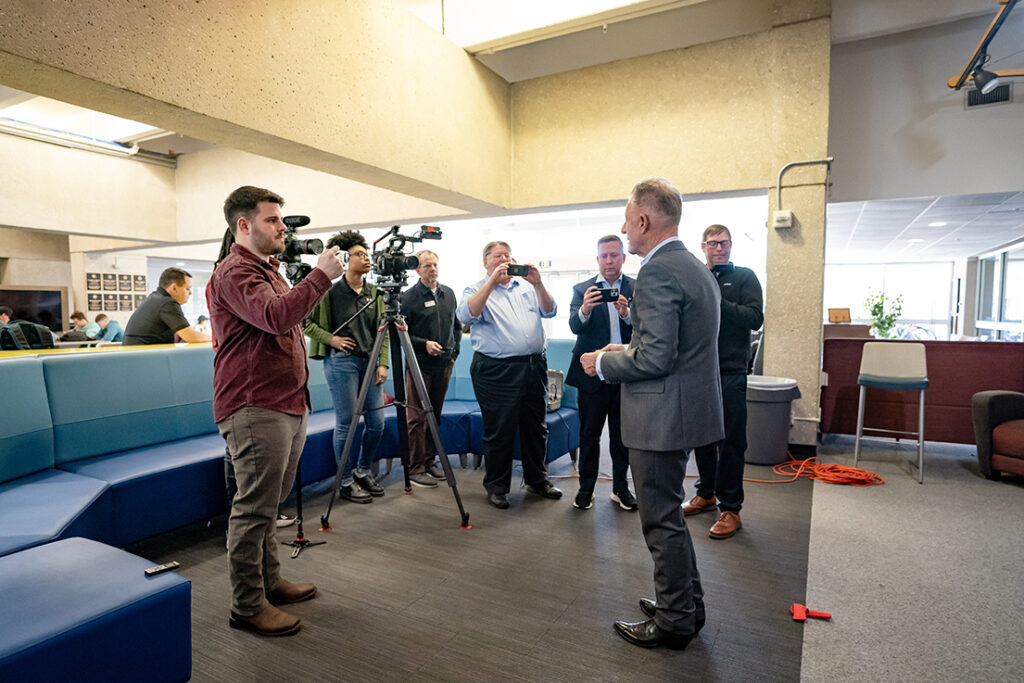 Seven members of local media hold cameras and smartphones as they interview singer-songwriter Lyle Lovett.
