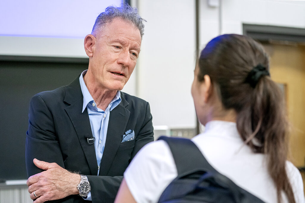 Singer-songwriter Lyle Lovett speaks to a college student in a classroom.