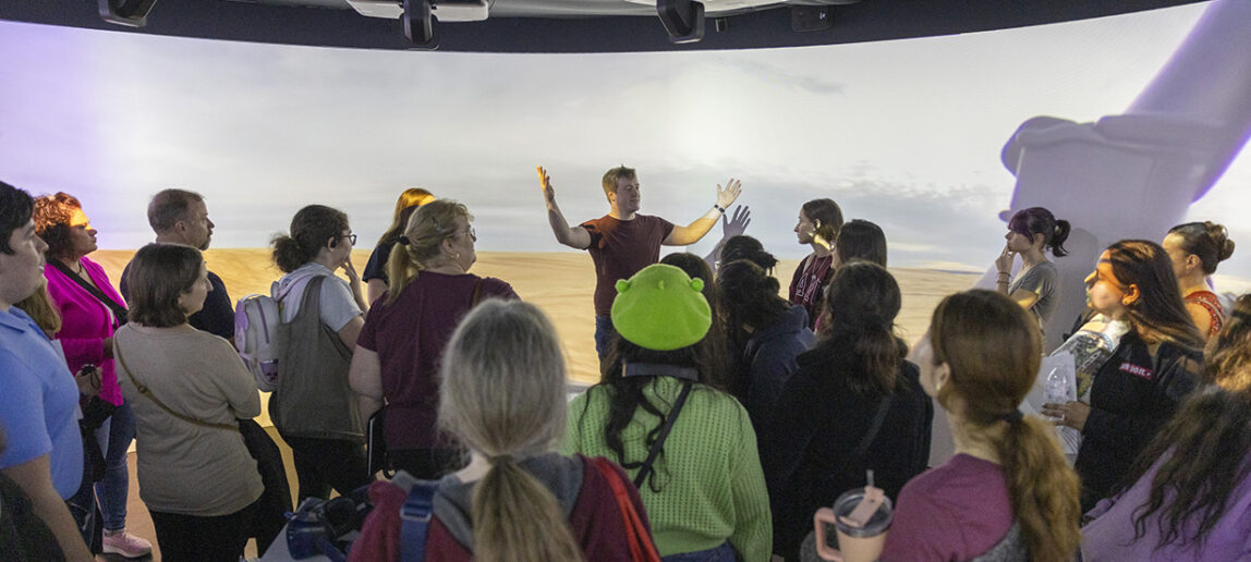 Students and family members gather in an immersive 360-degree screen environment as they listen to a presentation.