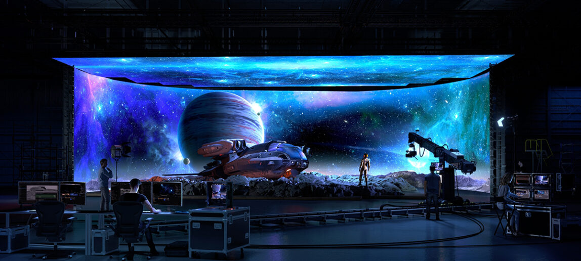 A virtual production stage is shown, with images of outer space. A starship and an actor are in front of the screen. In the foreground are people working on filming the scene.
