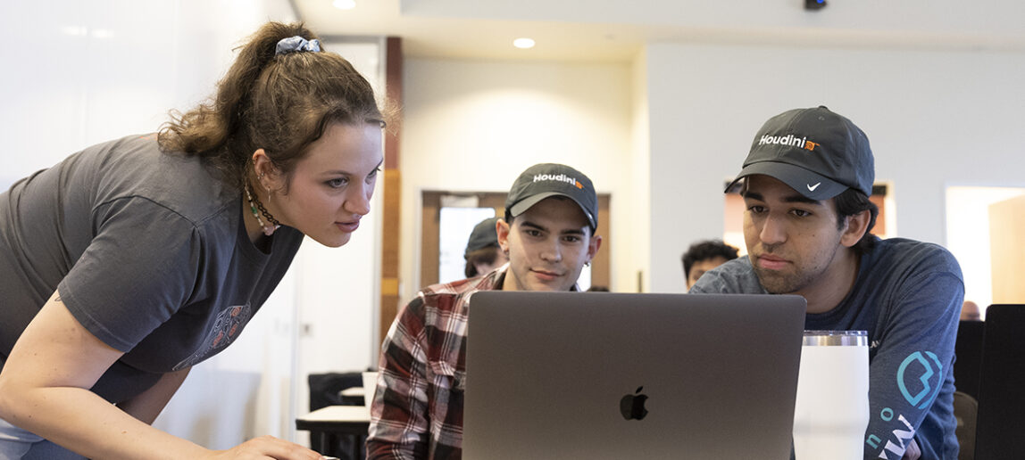 Two students look at their computers, along with a software professional.