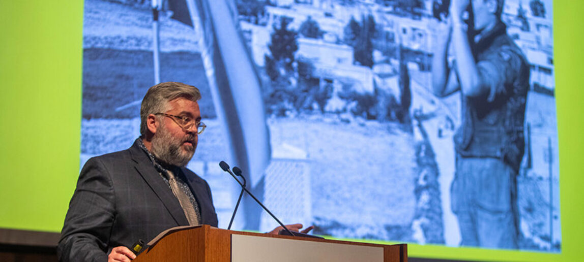 A professor stands at a podium, giving a presentation.