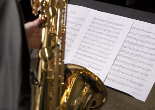 A closeup of sheet music, with a student playing saxophone in front of it.