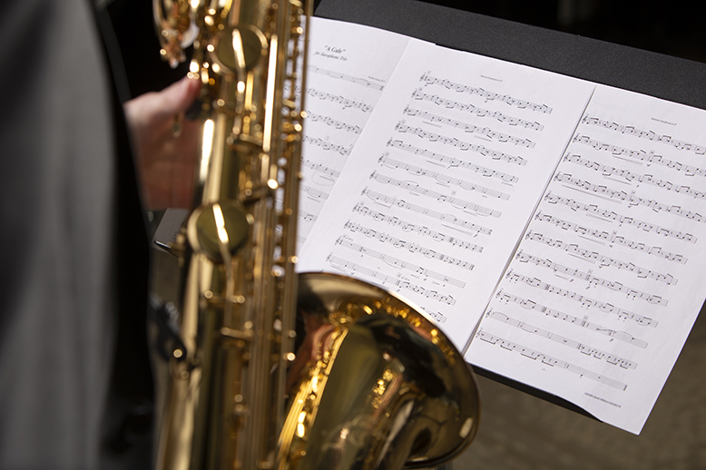 A closeup of sheet music, with a student playing saxophone in front of it.