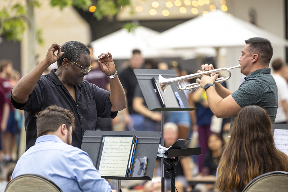 A conductor leads a brass ensemble, including a trumpet player.