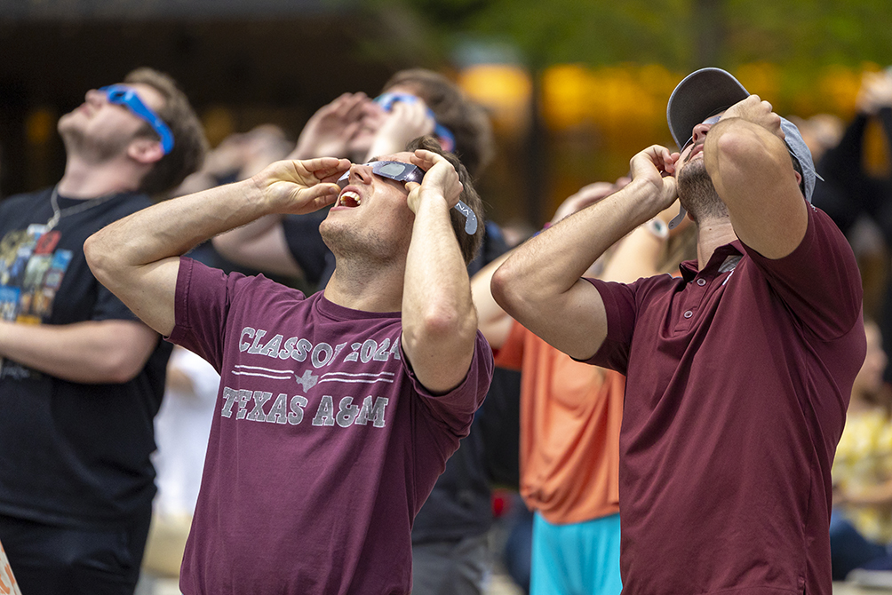 College students wearing solar glasses look up toward the sky during the solar eclipse.