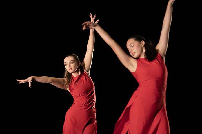 Two members of a high school dance troupe, both wearing red, are shown performing onstage.