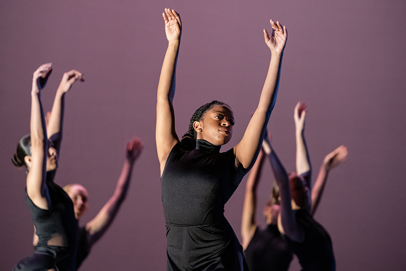 Five members of a high school dance troupe are shown, all reaching their arms upward.