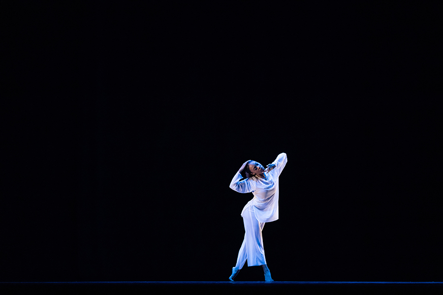 A solo dance performer wearing white is shown onstage.