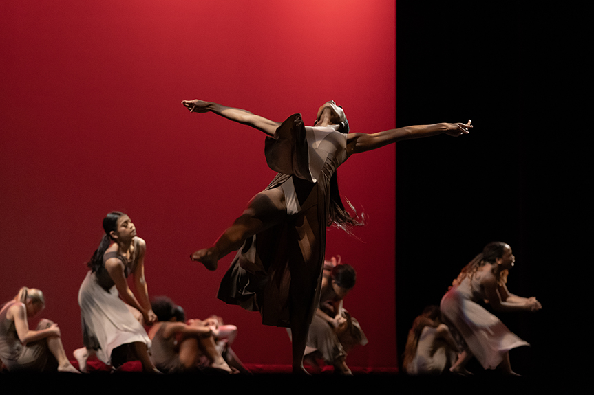 A high school dance company performs onstage, backed by a red screen.