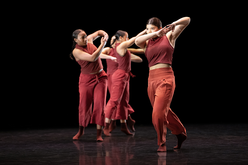 Four high school dance students, all wearing red, perform in sync with each other onstage.