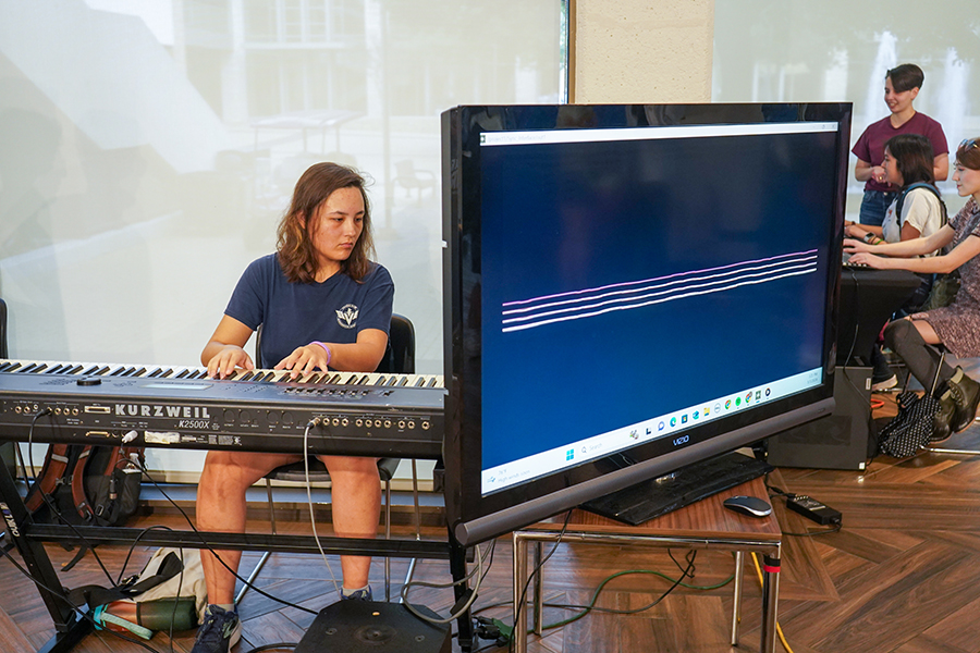 A college student plays a keyboard, with a screen showing lines that are connected to the notes being played.