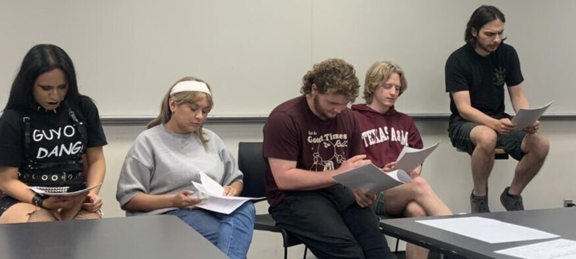 Five students sitting in a classroom in a screenwriting class look at their screenplays.