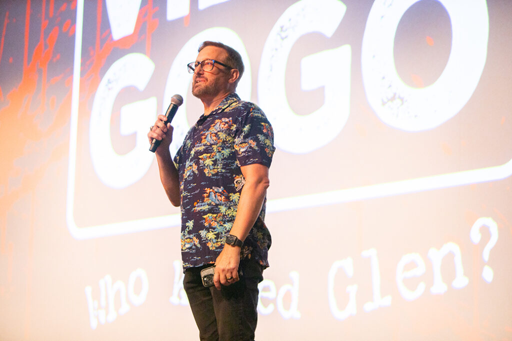 A college professor speaks into a microphone on a stage.