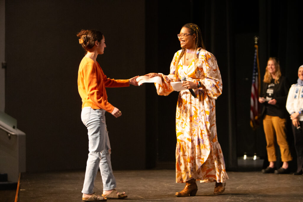 A college professor hands an award certificate to a college student.