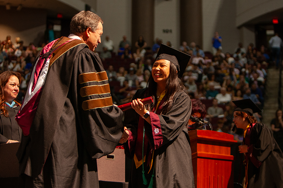 A college student receives a diploma onstage at a graduation ceremony.