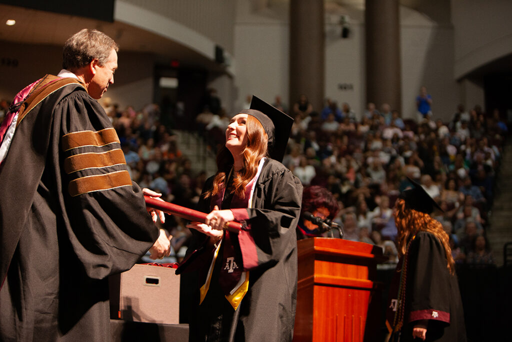 A college student receives a diploma onstage at a graduation ceremony.