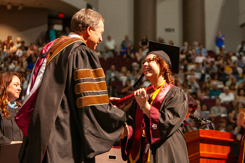 A college student receives a diploma onstage at a graduation ceremony.