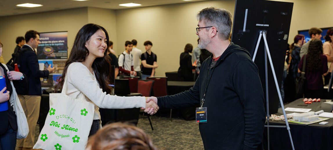 A college student shakes the hand of an industry professional during a career fair.