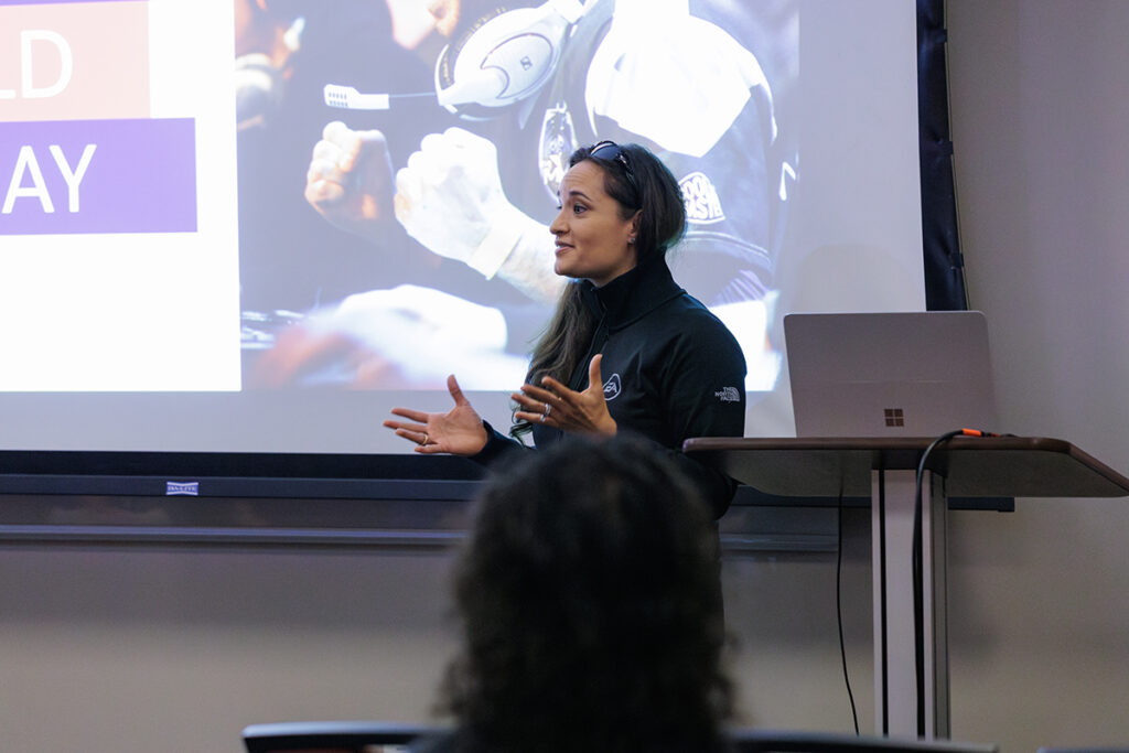 A video game professional stands in front of a screen during a presentation and speaks to college students in the audience.