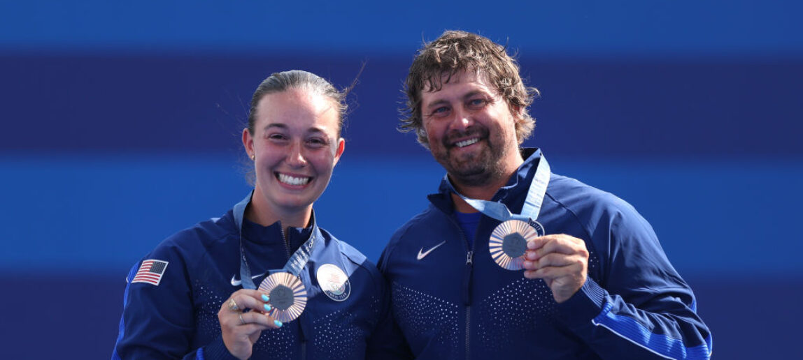 Two Olympic archers hold their bronze medals and smile at the Olympic Games in Paris.