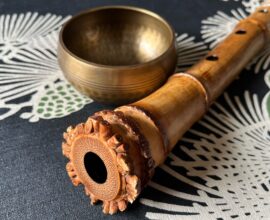 A shakuhachi, an end-blown bamboo flute, is shown on a table with a decorative design and a gold bowl.