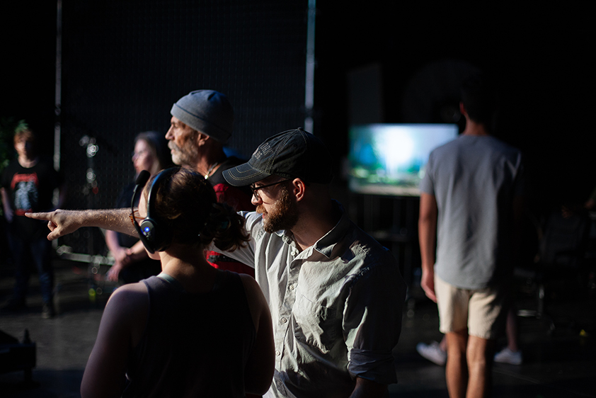 A college professor points toward a virtual production stage as he instructs a student on his left.