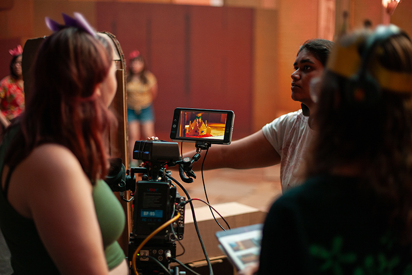 College students stand on a virtual production stage, looking at an image of a crown being displayed on a smartphone.