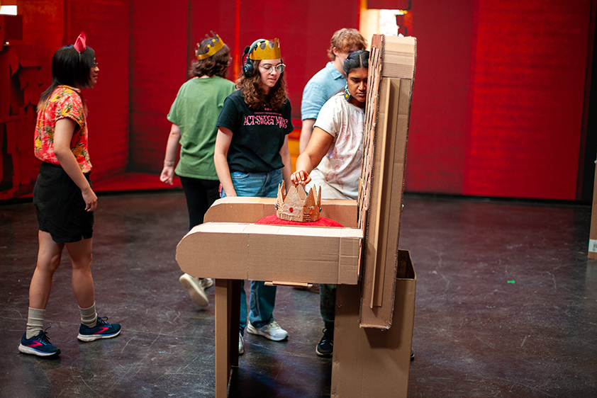 A cardboard throne with a cardboard crown are shown on a virtual production stage, with college students working around it.