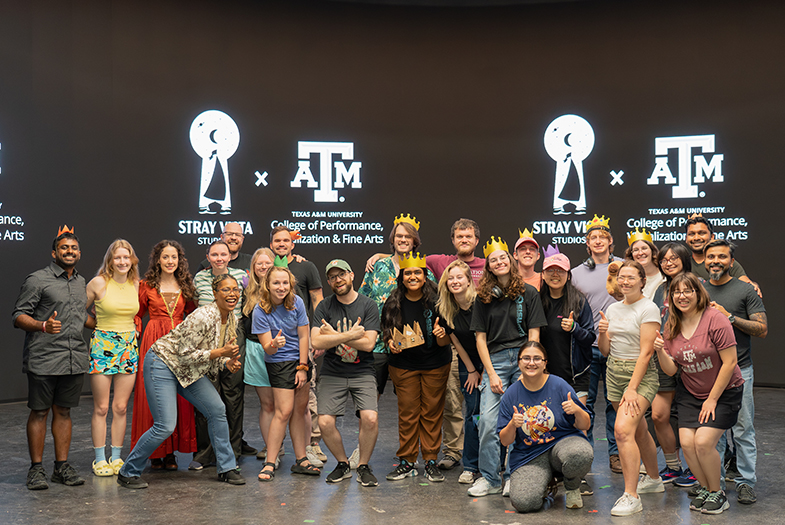 A group of college students, professors and industry professionals gather for a photo on a virtual production stage. On the large LED screen behind them are two logos: Stray Vista Studios and Texas A&M University College of Performance, Visualization and Fine Arts.