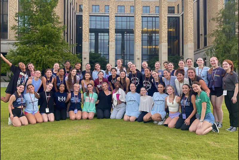 A group of high school dance students gather for a group picture outside of a university building.