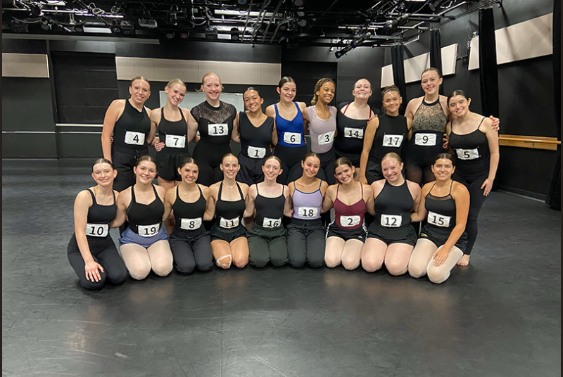 A group of high school dance students pose for a photo in a dance studio.