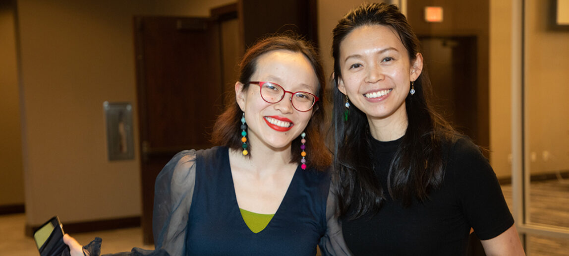 Two artists smile for a photo. Both are holding smartphones.