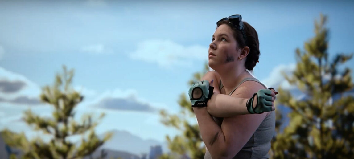 A still image from a short film features a woman wearing gloves and looking up in an outdoor setting. Behind her is the image of trees and sky from a large virtual production screen.