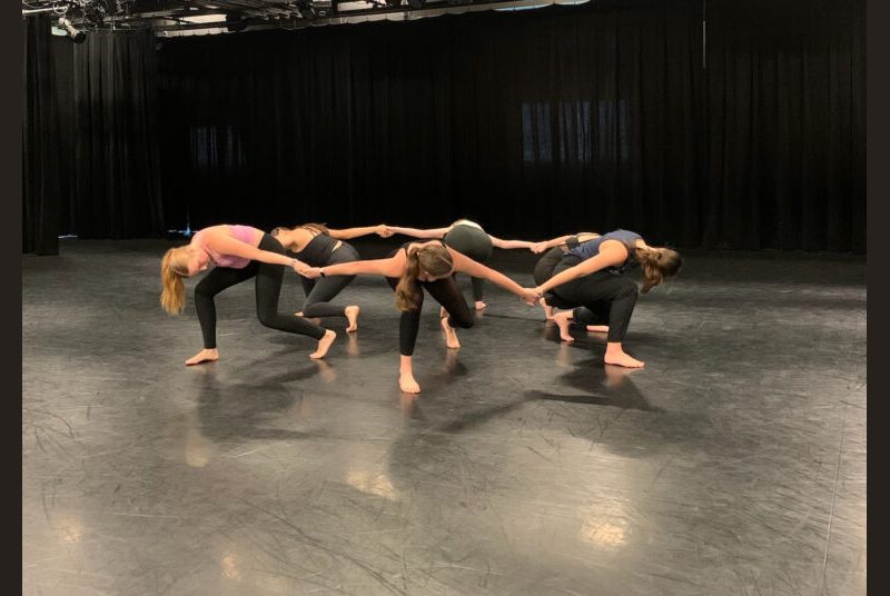 Six dancers are crouching down while holding hands in a circle pattern.