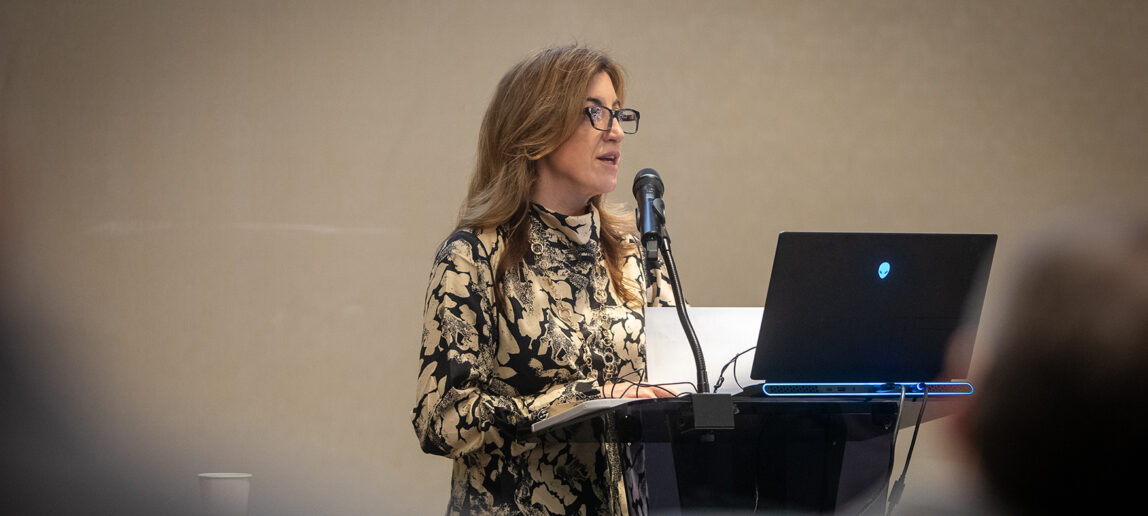 A woman speaks at a podium in a conference room.