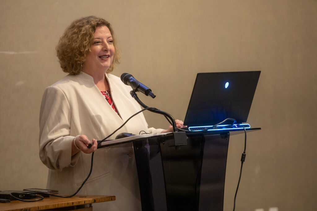 A university faculty member speaks at a podium in a conference room.