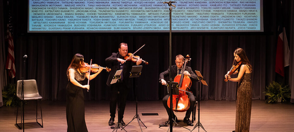 A string quartet performs onstage. Behind them, projected on the screen are the names of Japanese-Americans who were incarcerated during World War II