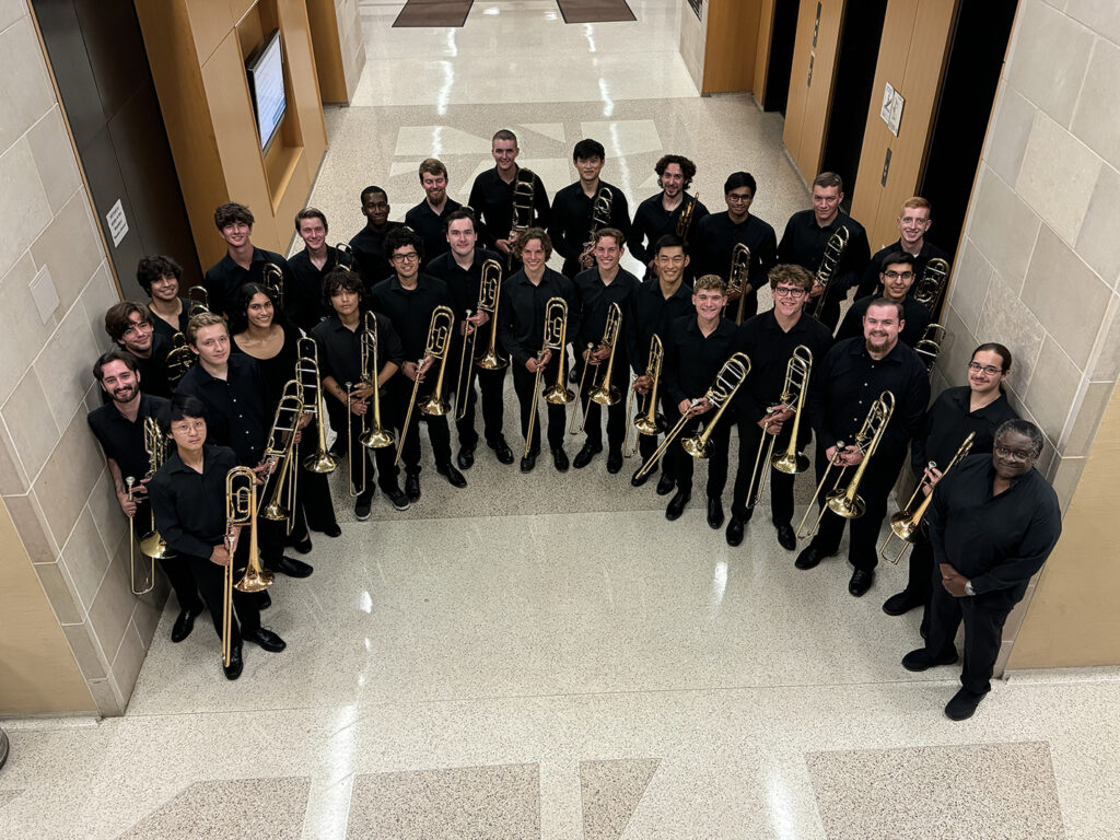 A group of musicians, all wearing black and holding trombones, smiles for a photo.