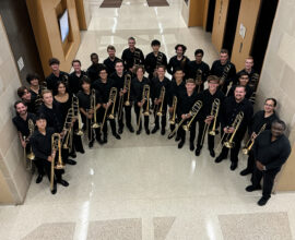 A group of musicians, all wearing black and holding trombones, smiles for a photo.